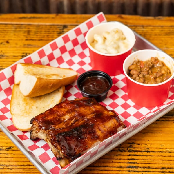 Hudson's Grill BBQ ribs with mac and cheese, baked beans, garlic bread, and BBQ sauce.
