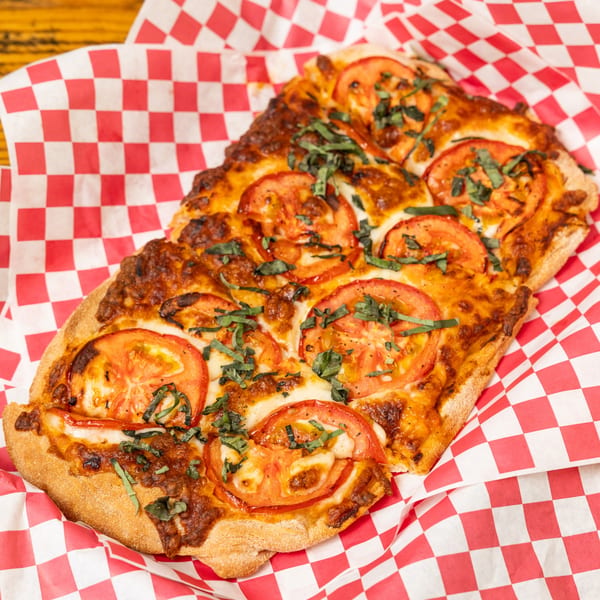 Hudson's Grill flatbread pizza with melted cheese, sliced tomatoes, and fresh basil on checkered paper.