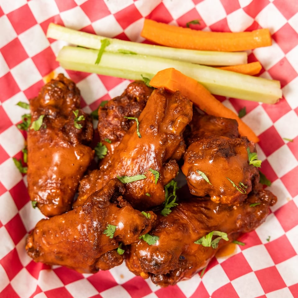 Hudson's Grill at Fig's BBQ chicken wings with celery and carrot sticks on red checkered paper.