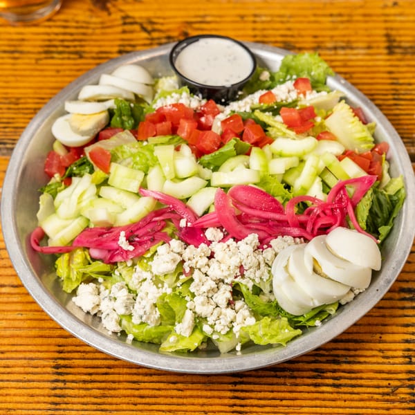 A vibrant Hudson's Grill salad with lettuce, tomatoes, cucumbers, pickled onions, hard-boiled eggs, and feta cheese.