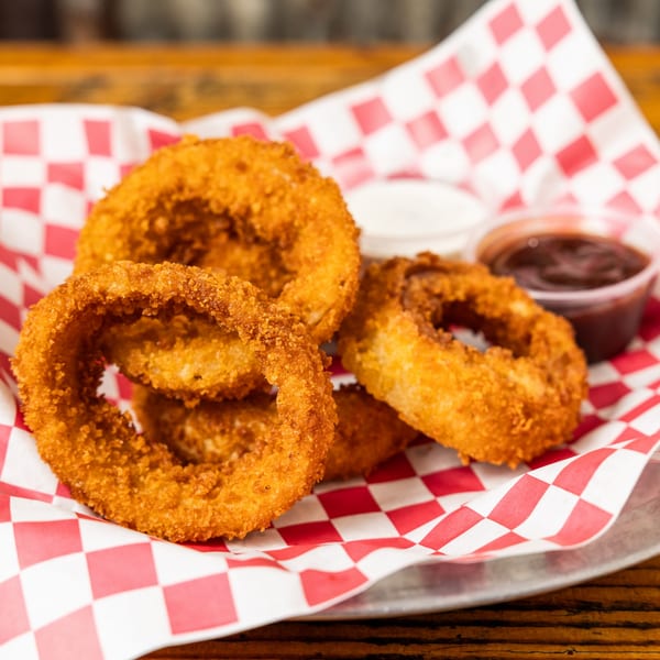 Crispy golden onion rings in a red and white checkered paper-lined basket with dipping sauces.