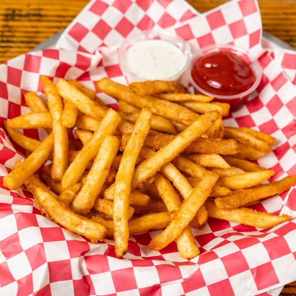 A basket of golden french fries with small containers of ketchup and ranch dressing.