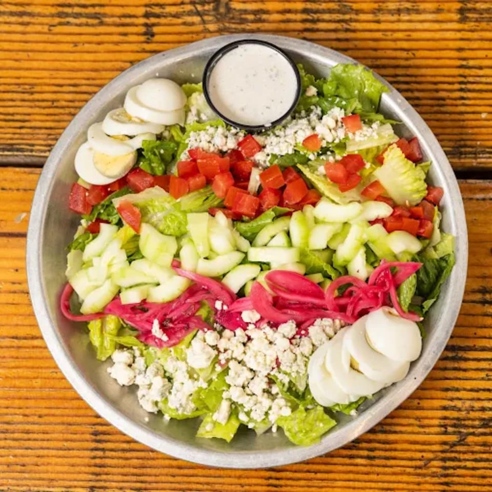 A vibrant Hudson's Grill salad with lettuce, tomatoes, cucumbers, pickled onions, blue cheese, and hard-boiled eggs.